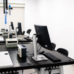 Laboratório de eletrônica com computadores, monitores e equipamentos técnicos sobre bancadas
