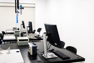 Laboratório de eletrônica com computadores, monitores e equipamentos técnicos sobre bancadas