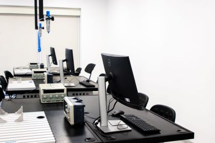 Laboratório de eletrônica com computadores, monitores e equipamentos técnicos sobre bancadas