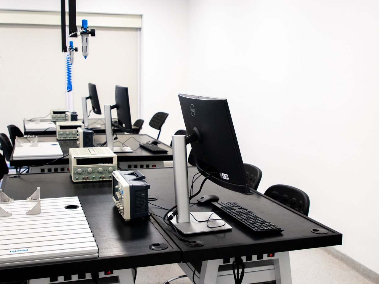Laboratório de eletrônica com computadores, monitores e equipamentos técnicos sobre bancadas