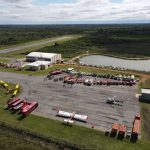 Vista aérea de uma base de combate a incêndios em Mato Grosso, com caminhões, helicópteros e aviões de emergência.