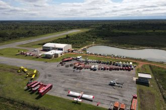 Vista aérea de uma base de combate a incêndios em Mato Grosso, com caminhões, helicópteros e aviões de emergência.