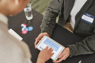Pessoa preenchendo um formulário de registro eleitoral em um tablet durante atendimento em uma estação de votação
