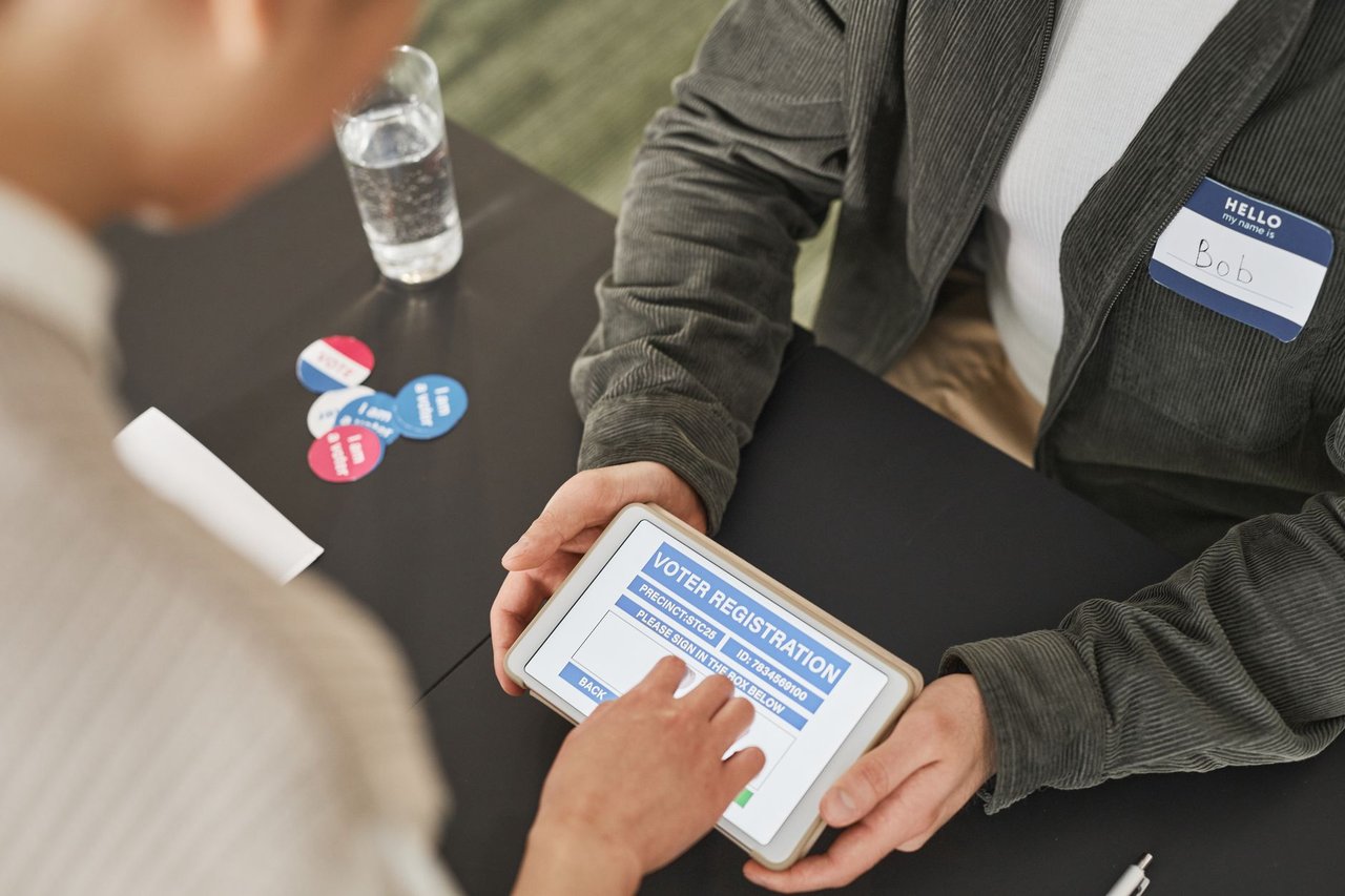 Pessoa preenchendo um formulário de registro eleitoral em um tablet durante atendimento em uma estação de votação