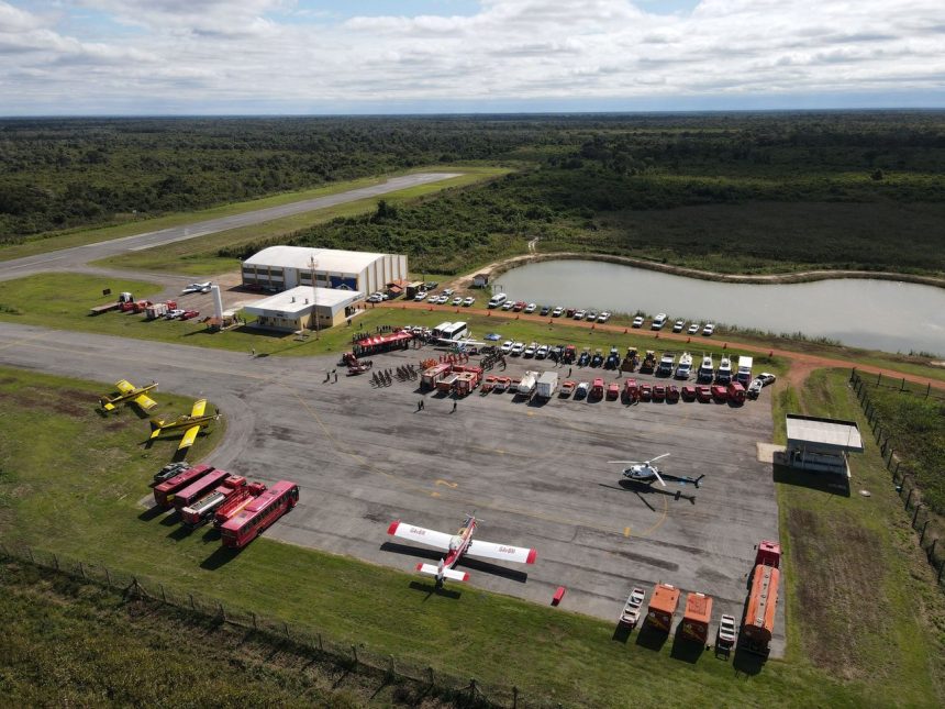 Vista aérea de uma base de combate a incêndios em Mato Grosso, com caminhões, helicópteros e aviões de emergência.