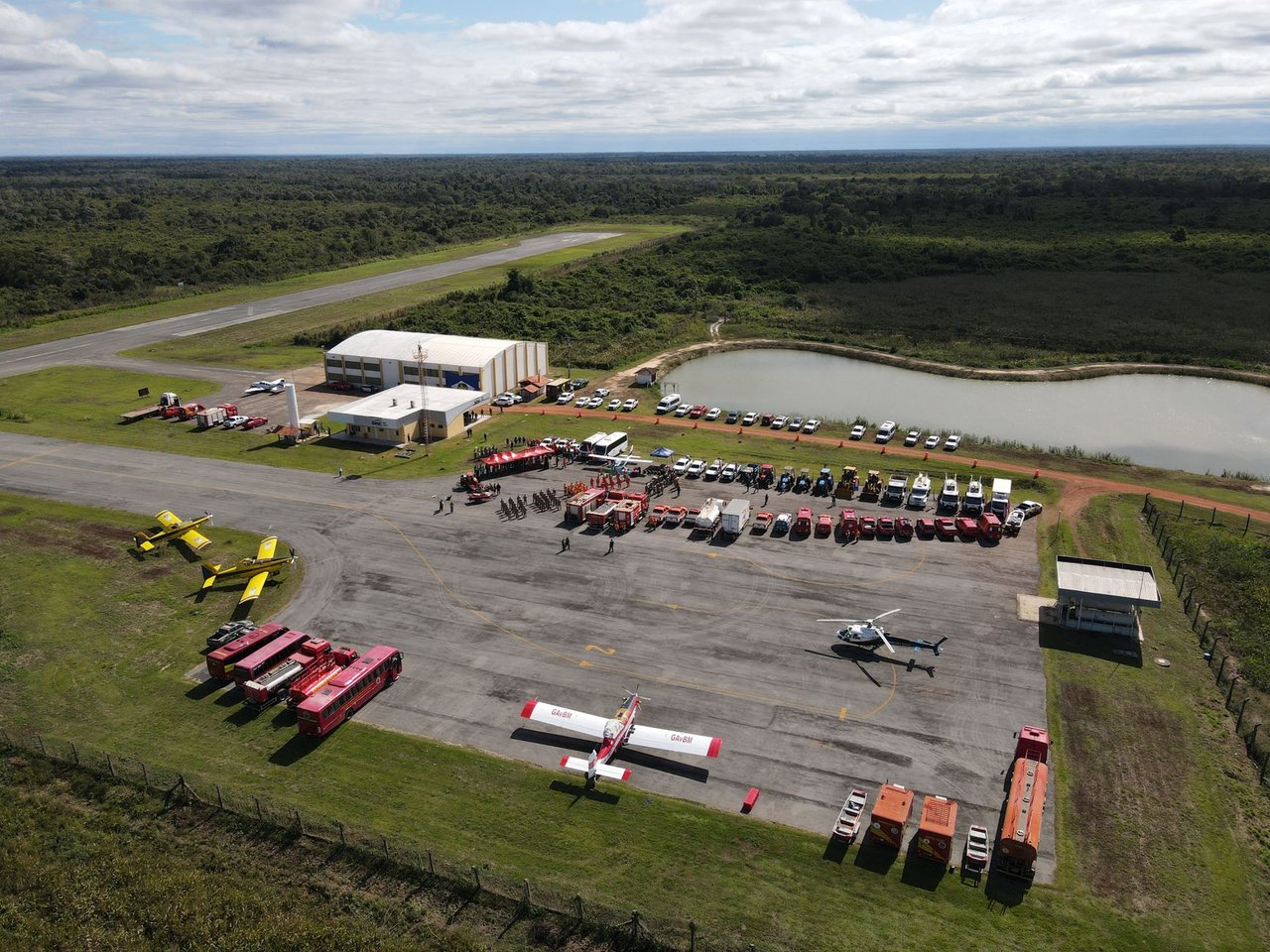 Vista aérea de uma base de combate a incêndios em Mato Grosso, com caminhões, helicópteros e aviões de emergência.