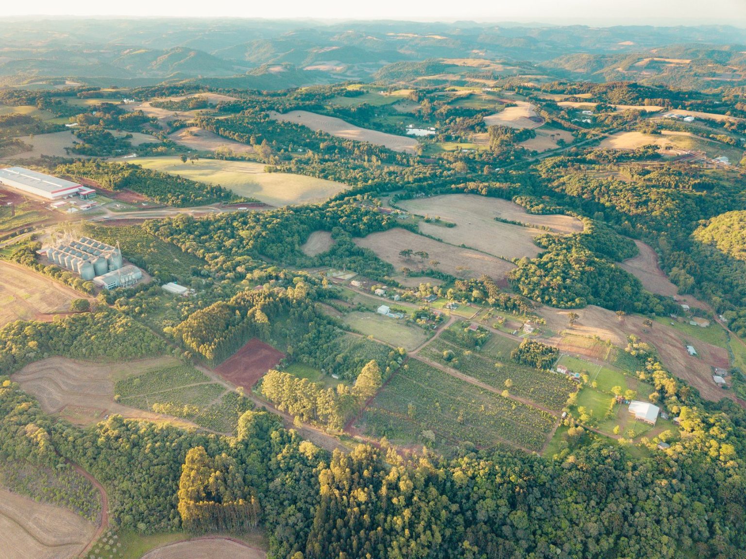 Vista aérea de áreas agrícolas e do campo no Centro do Rio Grande do Sul, durante o dia.